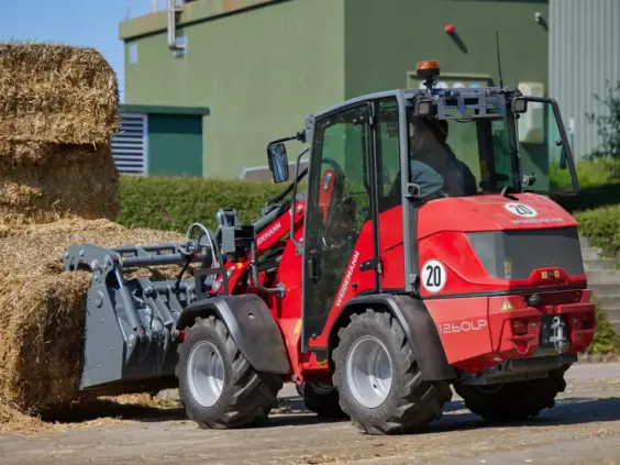 Rød Weidemann Hoftrac 1260LP minilaster som flytter store halmballer på en gård.