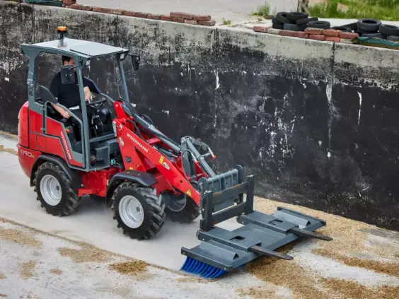En rød Weidemann Hoftrac 1190e minilaster med feiebørste på en betongplass.