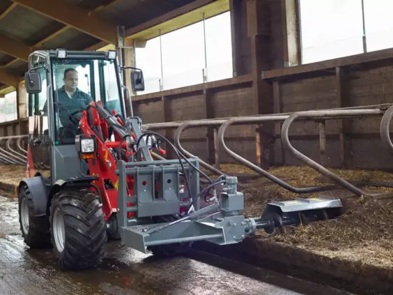 Weidemann Hoftrac 1160 minilaster i fjøsarbeid med et fôringstilbehør.