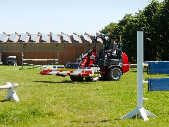 En Weidemann Hoftrac 1160 minilaster flytter fargerike hinderbommer på en gressbane.