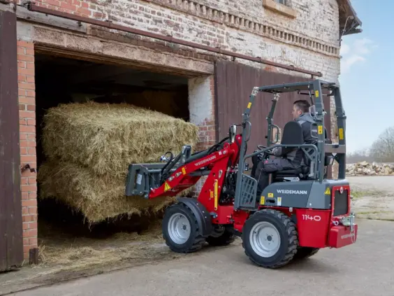 En Weidemann Hoftrac 1140 minilaster løfter en stor høyball ut av en låve.