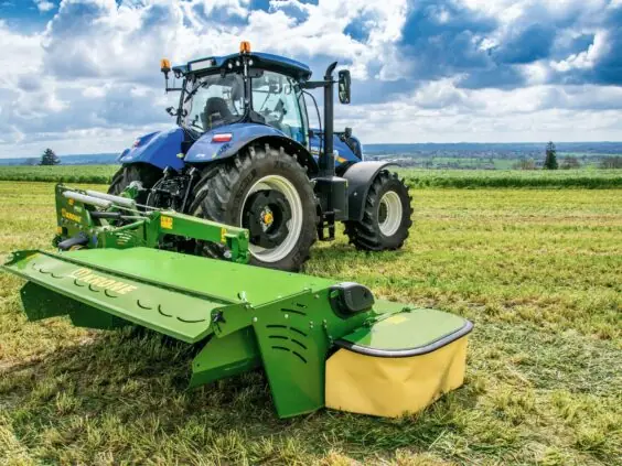 En blå traktor med en grønn Krone EasyCut R slåmaskin på en åker.