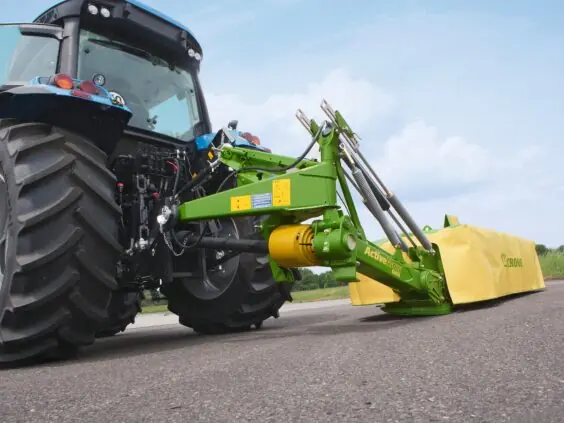 En Krone ActiveMow slåmaskin montert bak på en blå traktor på asfalt.