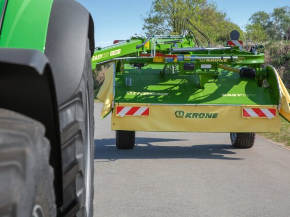 En KRONE EasyCut TS/TC slåmaskin på en vei bak en grønn traktor.