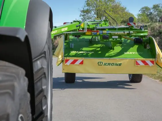 En KRONE EasyCut TS/TC slåmaskin på en vei bak en grønn traktor.