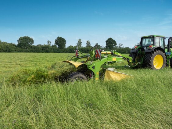 En traktor som trekker en KRONE EasyCut TS/TC slåmaskin gjennom et grønt gressfelt.