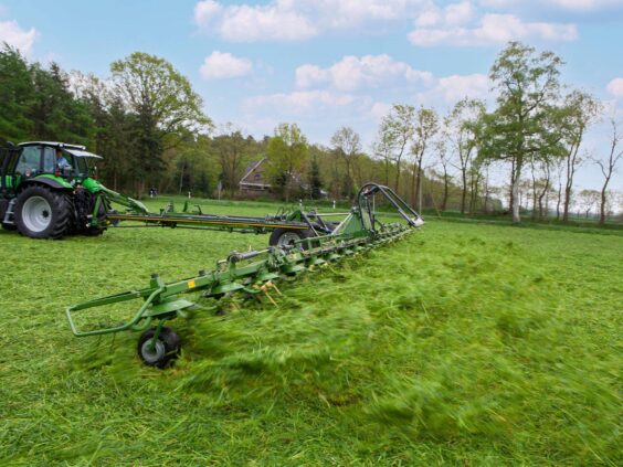 En grønn traktor som bruker en KRONE KWT-serie vender på en gresskledd åker.