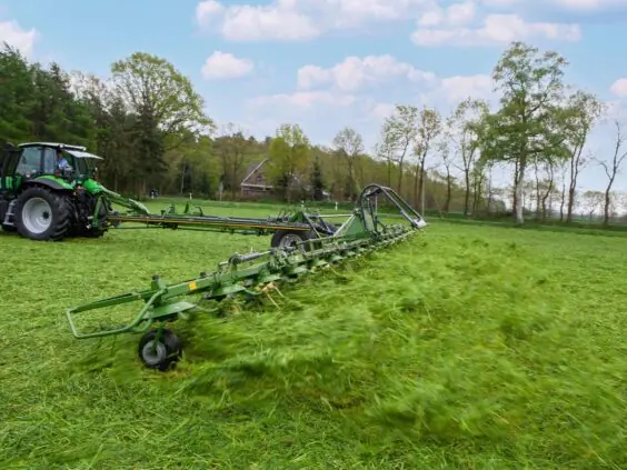 En grønn traktor som bruker en KRONE KWT-serie vender på en gresskledd åker.