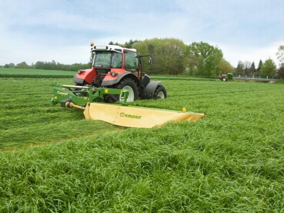 Rød traktor i arbeid på grønn eng med en Krone EasyCut R slåmaskin.
