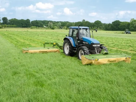 Blå traktor i arbeid på gressfelt med en grønn Krone EasyCut R slåmaskin.