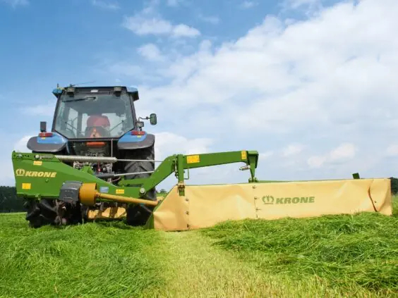 En blå traktor som bruker en Krone EasyCut R slåmaskin på et grønt jorde.