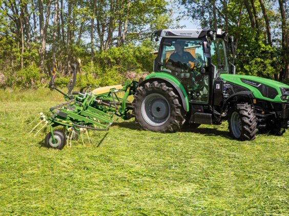Grønn traktor som trekker en KRONE Vendro vendespreder på en gressmark.