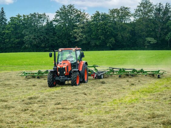 En oransje traktor som trekker en grønn KRONE Vendro vender på en gressmark.