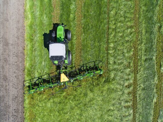 Grønn traktor med KRONE Vendro sprederive i arbeid på en frodig gressmark.