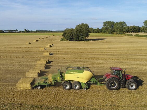 Rød traktor med en KRONE BaleCollect som samler firkantballer på en åker.