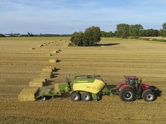 Rød traktor med en KRONE BaleCollect som samler firkantballer på en åker.