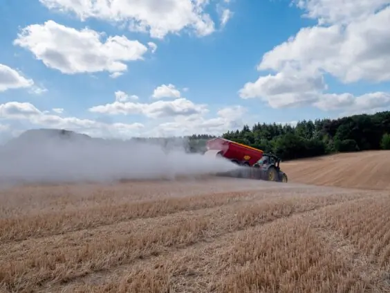 En traktor sprer kalk på en høstet kornåker under en blå himmel med skyer.
