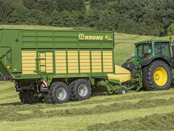 En grønn traktor som trekker en KRONE AX lessevogn på et gressjorde.
