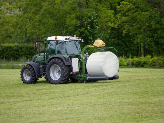 Grønn traktor på et jorde med en KRONE EasyWrap 150 som pakker en rundball.