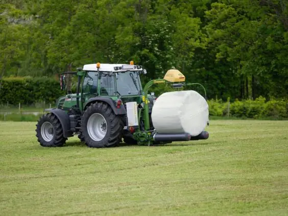 Grønn traktor på et jorde med en KRONE EasyWrap 150 som pakker en rundball.