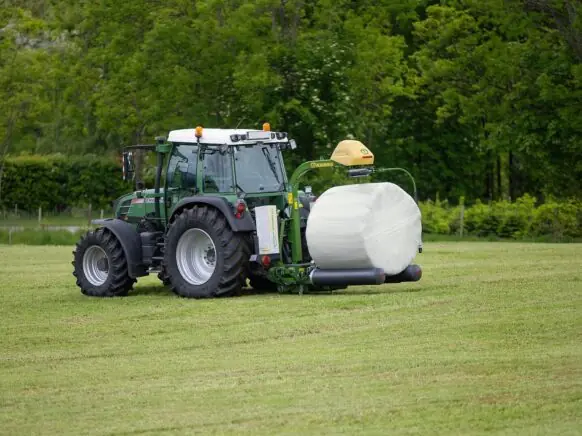 Grønn traktor på et jorde med en KRONE EasyWrap 150 som pakker en rundball.