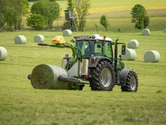 En traktor som pakker en rundballe med KRONE EasyWrap 150 på et jorde.