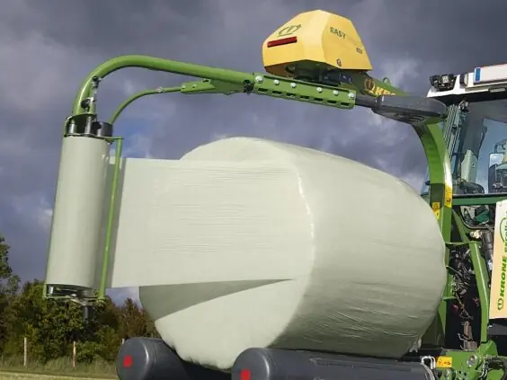 KRONE EasyWrap 150 rundballepakker som pakker en rundballe i lysegrønn plast på jordet.