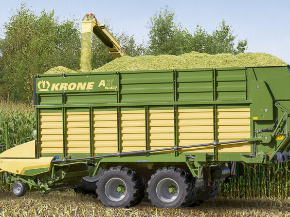 En grønn og gul KRONE AX lessevogn blir fylt med snittet mais på åkeren.
