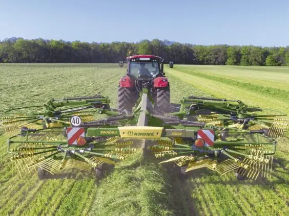 Rød traktor med KRONE Swadro TC samlerive på et grønt jorde i solskinn.