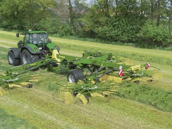 En grønn traktor trekker en KRONE Swadro TC samlerive på et gressfelt.