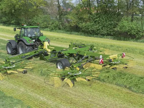 En grønn traktor trekker en KRONE Swadro TC samlerive på et gressfelt.