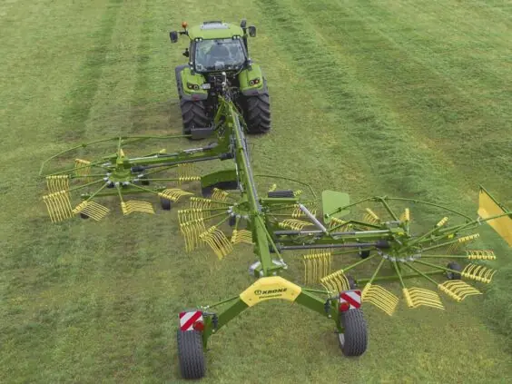 Grønn traktor som trekker en KRONE Swadro S | TS samlerive over et gressjorde.