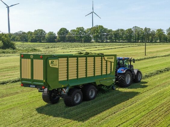En blå traktor som trekker en grønn KRONE RX lessevogn på et jorde.