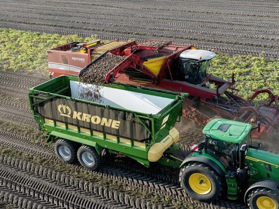 En grønn KRONE GX lessevogn fylles med poteter fra en landbruksmaskin på åkeren.