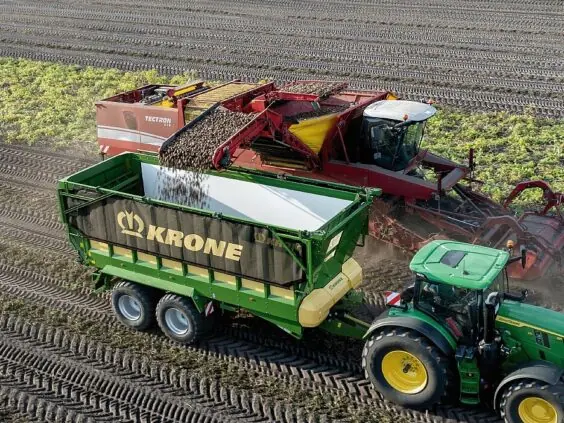En grønn KRONE GX lessevogn fylles med poteter fra en landbruksmaskin på åkeren.