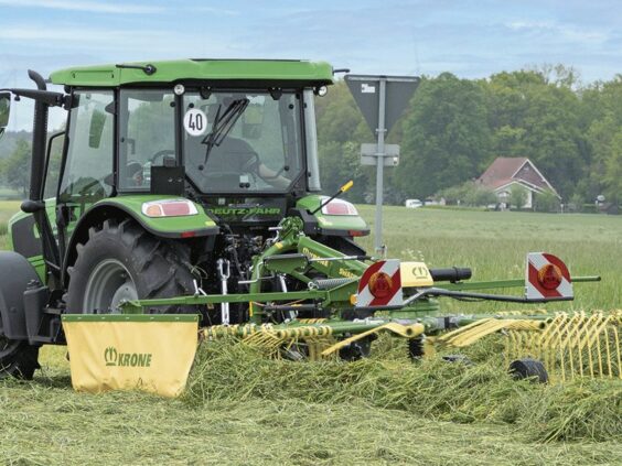 Grønn traktor med en KRONE Swadro S | TS samlerive i arbeid på en gresseng.