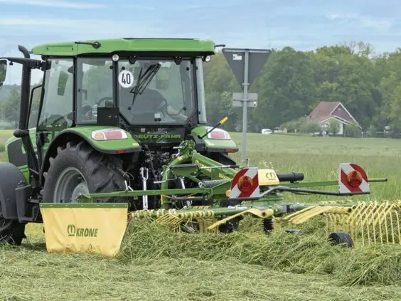 Grønn traktor med en KRONE Swadro S | TS samlerive i arbeid på en gresseng.