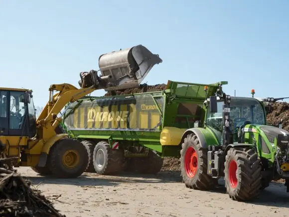 Hjullaster som fyller en grønn KRONE GX lessevogn trukket av en Fendt traktor.