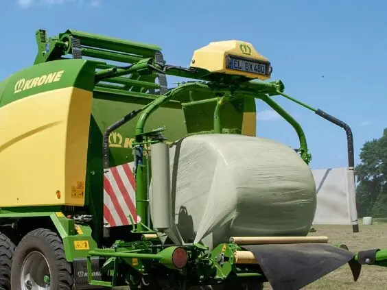 En Krone Comprima rundballepresser som pakker inn en rundballe i plast på et jorde.