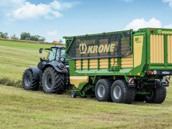 En traktor i arbeid med en KRONE MX lessevogn på et grønt jorde.