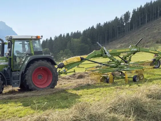 Fendt-traktor i arbeid med en KRONE Swadro S | TS samlerive på en eng.