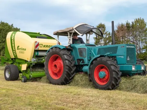 En Hanomag traktor trekker en Krone Fortima rundballepresser på et grønt jorde.