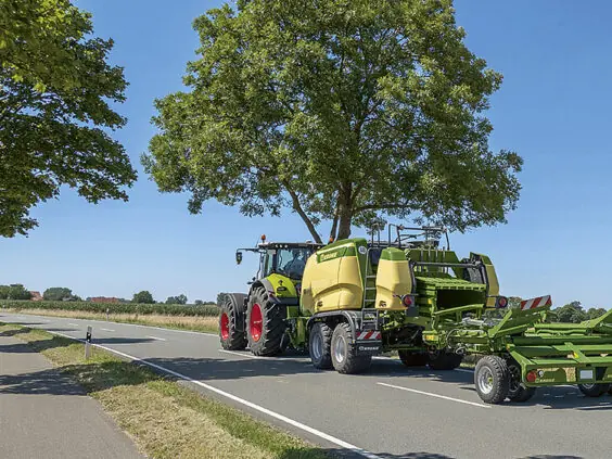 Grønn traktor på veien som tauer en ballepresse med KRONE BaleCollect.