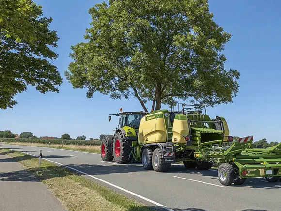 Grønn traktor på veien som tauer en ballepresse med KRONE BaleCollect.