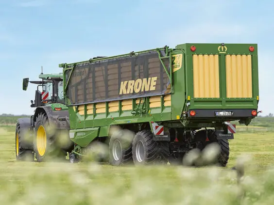 En grønn KRONE ZX lessevogn trekkes av en traktor på en grønn eng.