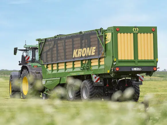 En grønn KRONE ZX lessevogn trekkes av en traktor på en grønn eng.