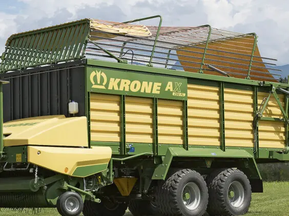 En moderne KRONE AX lessevogn i grønt og gult på en gresskledd åker.