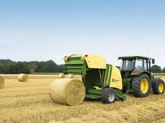 En traktor med Krone Bellima rundballepresser som lager halmballer på et gult jorde.
