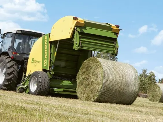 En Krone Bellima rundballepresser som slipper ut en fersk rundballe på et jorde.