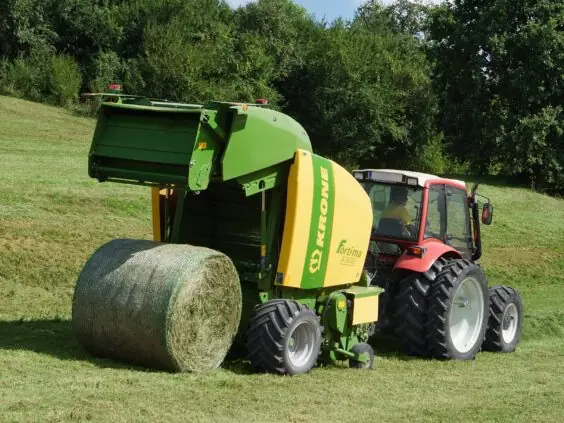 Rød traktor med Krone Fortima rundballepresser som slipper ut en fersk rundballe på jordet.